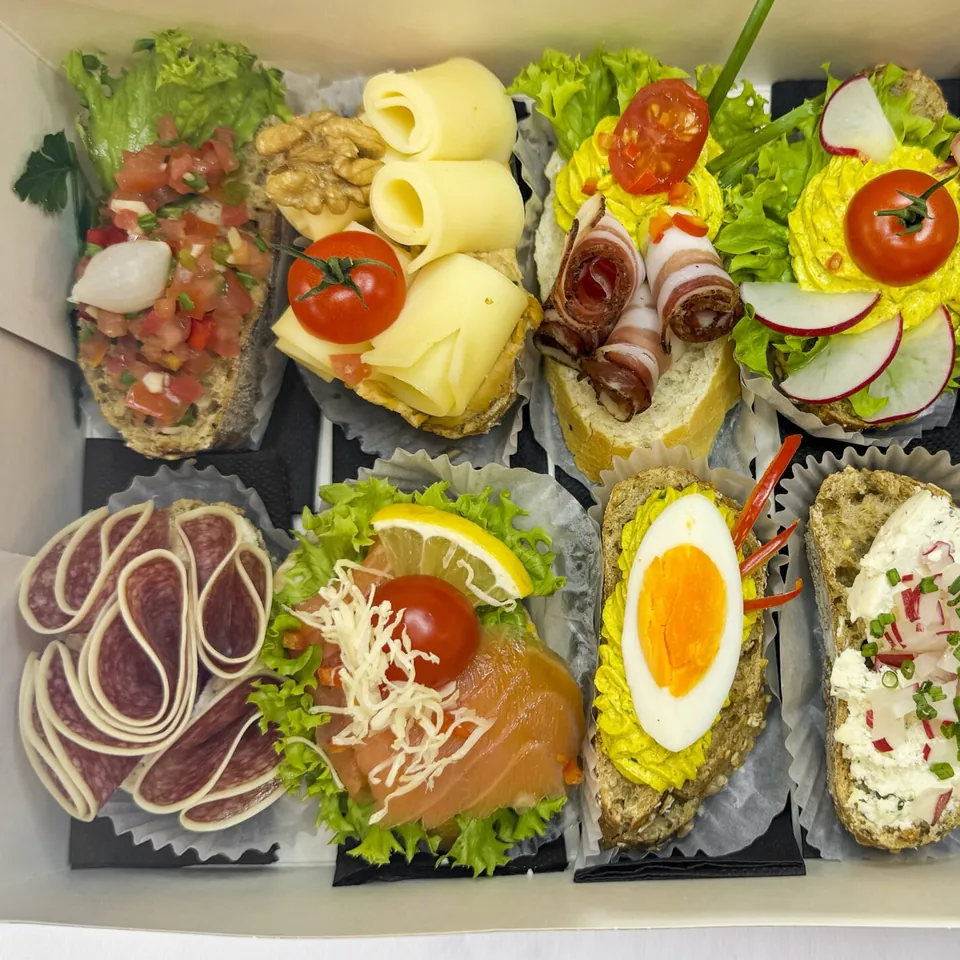 Geöffnete Box mit belegten Canapés: Lachs, Ei, Käse, Speck und Aufstriche auf Brot
